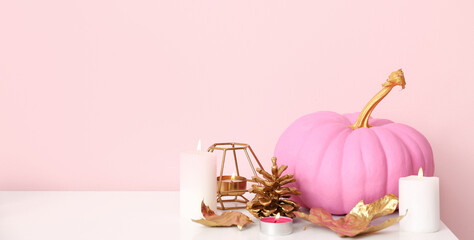 Wall Mural - Pink painted pumpkin with autumn leaves and burning candles on white table near color wall