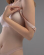 © Vitte Yevhen - In a minimalist studio, a person is adjusting the strap of a nude bra, showcasing the garment's design and fit against a soft, neutral backdrop.