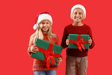 Wall Mural - Little children in Santa hats with Christmas presents on red background