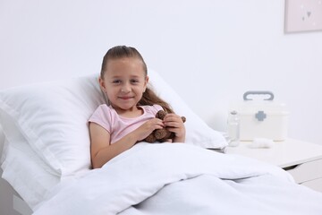 Canvas Print - Cute little girl with teddy bear on bed in hospital