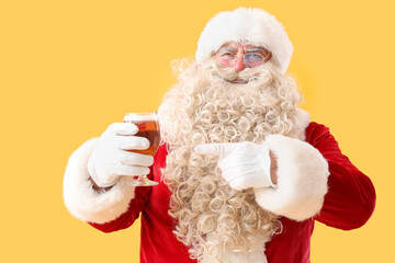 Canvas Print - Santa Claus pointing at glass of beer on yellow background