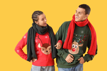 Wall Mural - Young couple in Christmas sweaters with scarves on yellow background