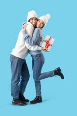 Wall Mural - Young women with Christmas gift hugging on blue background