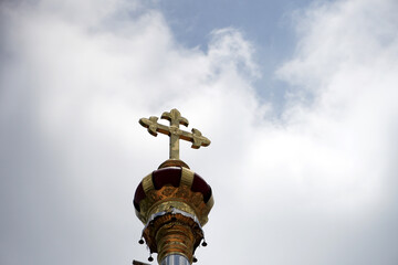 Golden cross on a church top with cloudy sky background.