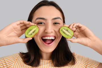 Poster - Beautiful young woman with fresh kiwi on grey background