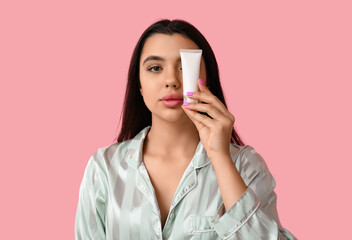 Wall Mural - Beautiful young woman with tube of cosmetic product on pink background