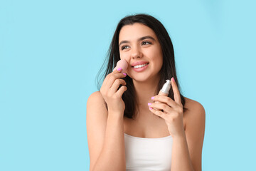 Wall Mural - Beautiful young woman with makeup sponge and liquid foundation on color background