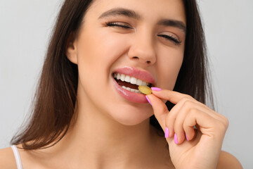 Poster - Woman with beautiful lips eating tasty candy on grey background, closeup