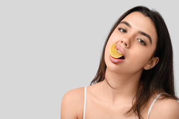 Sticker - Beautiful young woman with half of lemon in her mouth on grey background