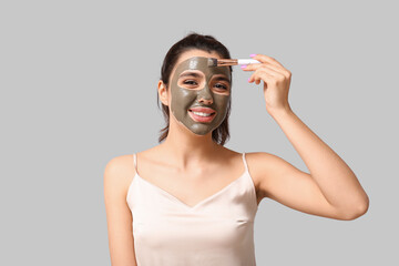 Wall Mural - Young woman applying facial mask on grey background