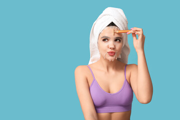 Sticker - Beautiful young woman with sheet facial mask using massage roller on color background