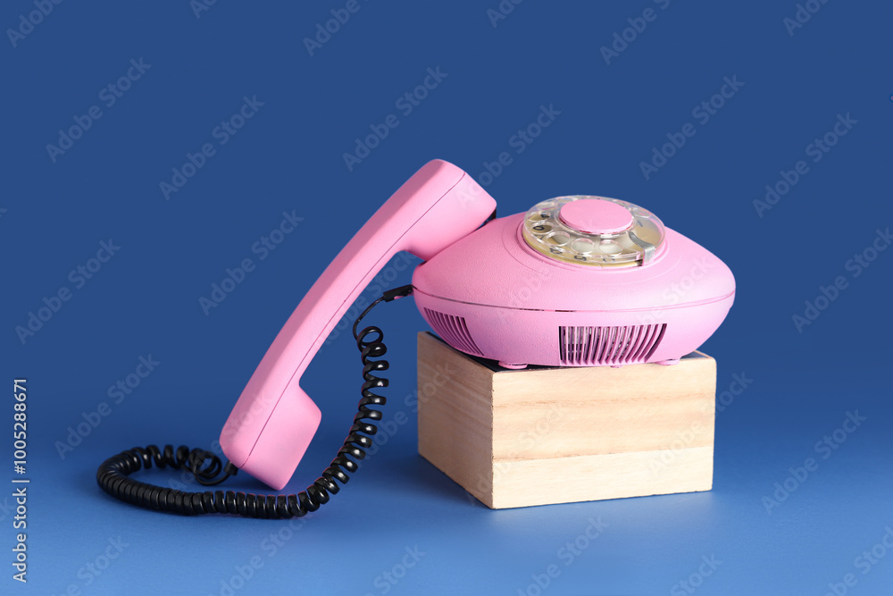 Wooden podium with pink retro telephone on blue background