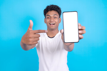 Young Indian Man Pointing While Showing Smartphone With Blank Screen For Mockup Over Blue Background