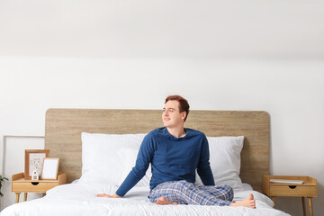 Canvas Print - Morning of handsome young happy man in stylish pajamas sitting on bed at home