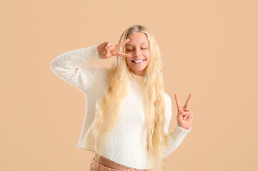 Canvas Print - Happy teenager girl showing victory gesture on beige background