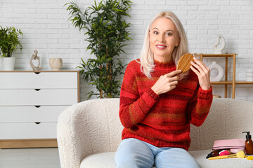 Canvas Print - Mature woman brushing hair while sitting on sofa at home