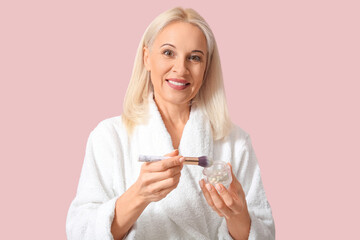 Poster - Mature woman in bathrobe with makeup powder and brush on color background