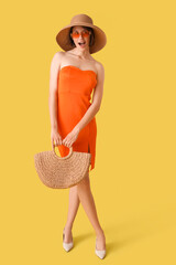 Wall Mural - Pretty young woman with sunglasses and handbag on yellow background