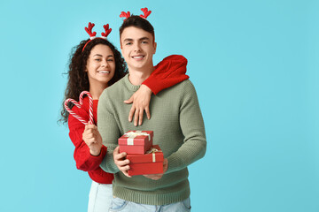 Wall Mural - Happy young couple in Christmas sweaters with candy canes and gift boxes on blue background