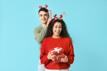 Wall Mural - Happy young couple in Christmas sweaters with candy canes and gift boxes on blue background