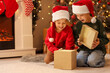 © Pixel-Shot - Cute happy little children in Santa hats opening gift box on Christmas eve at home