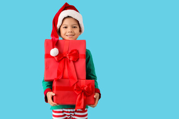 Poster - Cute happy little Asian boy in Santa hat dressed as elf with Christmas gift boxes on blue background