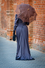 A woman in a long dress is walking down a brick street holding an umbrella