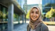 © MD Media - Beautiful muslim woman isolated against a city background business woman smiling in front of an office buildings. Young woman wearing a hijab. Middle eastern
