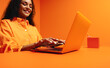 © Jacob Lund - Happy woman typing on laptop in vibrant, monochromatic orange office setting emphasizing creativity