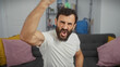 © Krakenimages.com - Fist-raising bearded man in white shirt shows excitement in a modern living room.