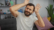 © Krakenimages.com - A middle-aged man with a beard shows discomfort in his cozy living room, holding an elbow.