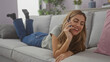 © Krakenimages.com - A cheerful young woman laying on a couch at home, chatting on a smartphone in a cozy room.