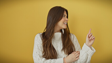 Canvas Print - Smiling young hispanic woman in white sweater over yellow background pointing and looking away.