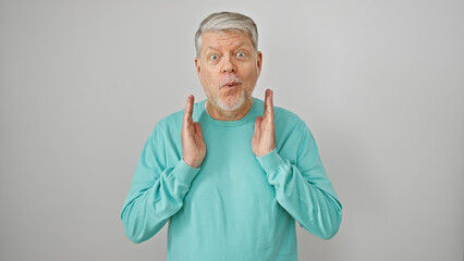 Wall Mural - Surprised senior man with gray hair in a turquoise sweater gesticulating against a white background.