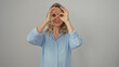 © Krakenimages.com - Playful blonde woman making glasses shape with hands against a white background, portraying curiosity and fun.