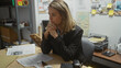 © Krakenimages.com - A contemplative blonde woman in a suit sits at a cluttered detective's desk in a police station, surrounded by case evidence and paperwork.