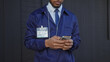 © Krakenimages.com - African american man in a uniform with an id badge using a smartphone on an urban street.