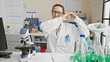© Krakenimages.com - A cheerful hispanic woman scientist making a heart gesture in a laboratory filled with scientific equipment.
