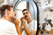 © Zoran Zeremski - Young man trims his mustache with scissors in the bathroom in front of the mirror.