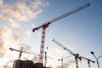 Poster - Cranes lift building materials at a busy construction site with an expansive sky filled with clouds during the afternoon