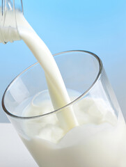 Fresh milk being poured into a glass on blue background