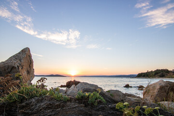 View through rocks on a sandy beach into the sunset. Landscape shot with a view to the horizon over the wide sea on the coast of Ouranoupoli, Thessaloniki, Central Macedonia, Greece