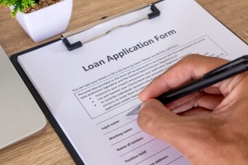 Close up view of hand holding pen to fill out loan application form