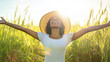 © wolfhound911 - A joyful Black woman wearing a wide brimmed sun hat, standing in a sunlit field of tall grass, arms outstretched, with the bright sun shining down from above.