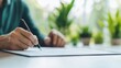 © Nopadon - A close-up of a person writing on a sheet of paper, surrounded by greenery, depicting productivity and focus in a serene environment.