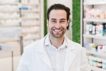 Handsome young male caucasian druggist pharmacist in white medical coat smiling and looking at camera in pharmacy drugstore