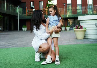 A woman kneels to talk to a young girl in a modern urban park during the afternoon