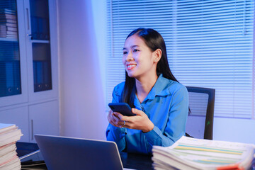 Asian businesswoman working hard in front of computer and many documents on desk at office late at night with serious action