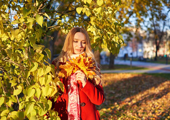 A woman in a red coat and a black skirt walks in an autumn park. The concept of autumn and the beauty of nature.