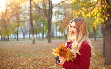 A woman in a red coat and a black skirt walks in an autumn park. The concept of autumn and the beauty of nature.